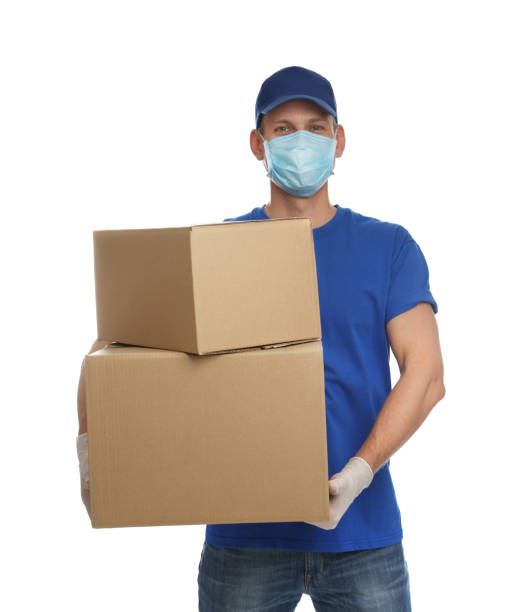 istock Courier in protective mask and gloves holding cardboard boxes on white background. Delivery service during coronavirus quarantine 1341258766