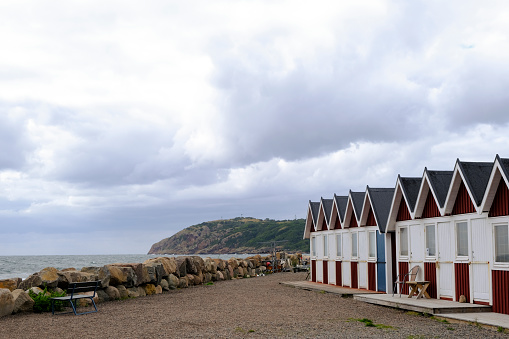 Molle, Sweden - August 19, 2021: Traditional red painted fishermen's houses in a row on the west coast of Sweden, cloudy day. In the distance Kullaberg Nature Reserve, Skane.
