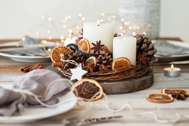 Rustic decor for christmas holiday family dinner. Center piece with white candle, dry orange, cones, cotton. Zero waste eco friendly home decoration. Cozy atmosphere, wooden background. Close up