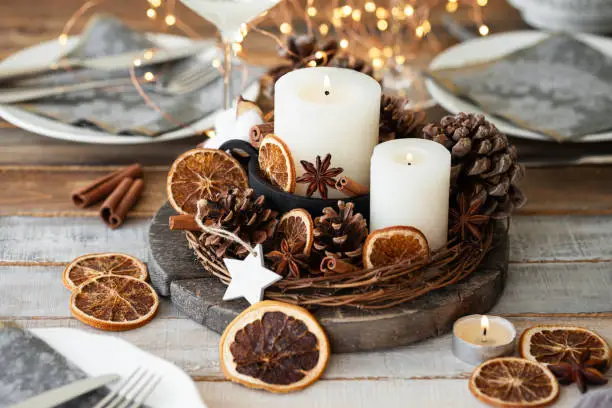 Photo of Rustic decor for christmas holiday family dinner. Center piece with white candle, dry orange, cones, cotton. Zero waste eco friendly home decoration. Cozy atmosphere, wooden background. Close up