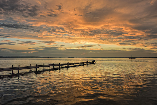 Rear view on young couple sitting on lakeside jetty at dusk with afterglow