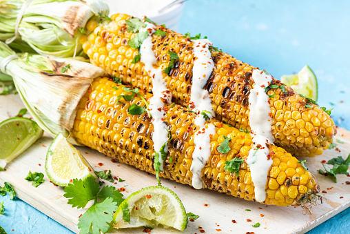 BBQ Grilled Whole Corn Cob. Served with HErbs, Lime and Salt on Wooden Board. Top View