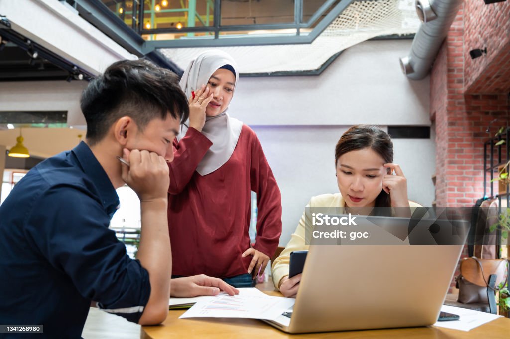 Business people under pressure at work desk Asian business colleagues getting stress trying to find solution for work problem at workstation. Discussion Stock Photo