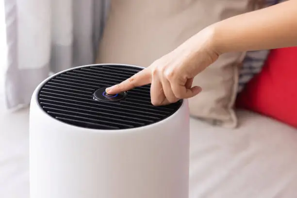 Close-up Asian woman hand, pressing a button on air purifier machine in a bedroom. dust and air pollution concept. air cleaner removing fine dust in house.