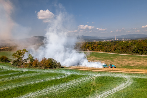 Aerial view of a tractor spreading lime on agricultural fields to improve soil quality after the autumn harvest. The use of lime powder to neutralize the acidity of the soil.