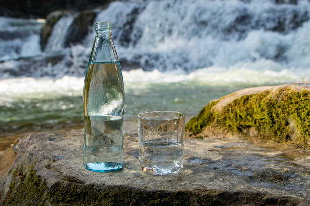 Natural drinking water in a bottle and glass beaker on nature background river.