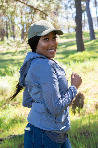 Young African woman with cap outdoors hiking jogging in forest smiling having fun
