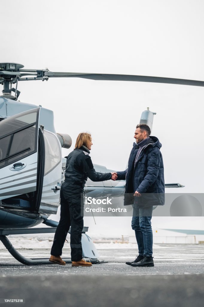 Chopper pilot greeting man with handshake Chopper pilot welcoming a male passenger on helipad. Pilot greeting man with handshake by the helicopter. Helicopter Pilot Stock Photo