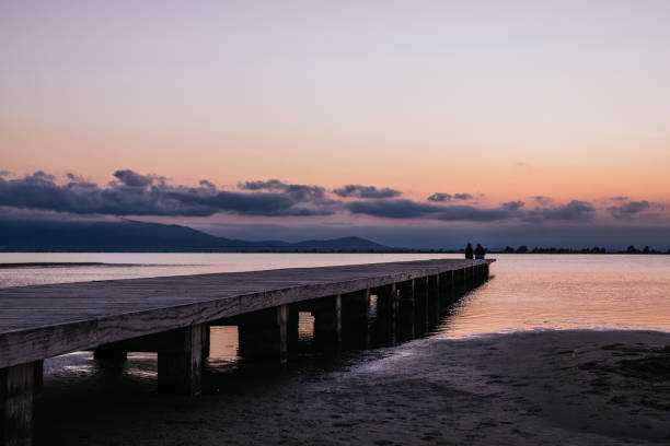 istock Anonymous persons sitting on pier near sea at sunset 1341275718