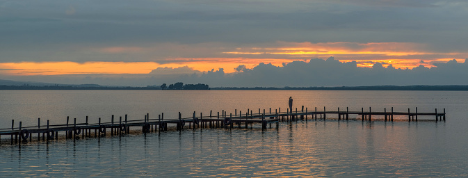 Silhouette of man standing on jetty at dusk with afterglow