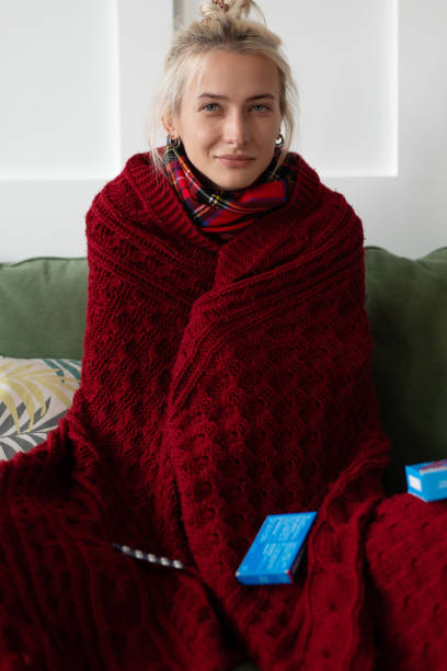 istock Woman with a cold is sitting on the couch wrapped in a plaid. 1341278105
