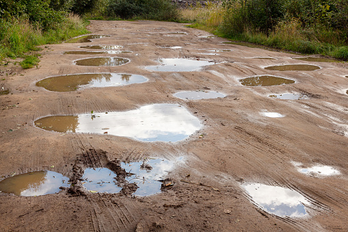 Many large deep puddles on uneven dirt sandy road with car wheel marks