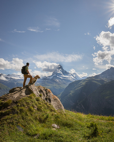 Hiker and dog admires the view of the Matterhorn from the path on a sunny summer day.