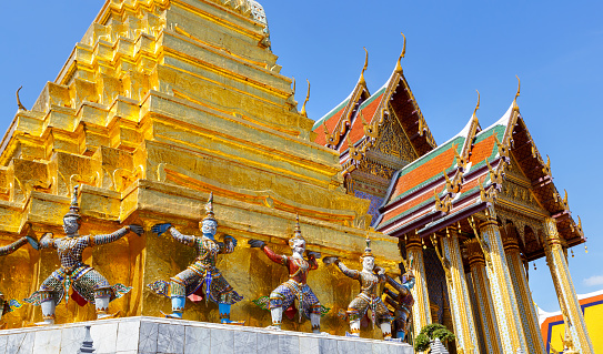 Golden pagoda with demon guardian at The Wat Phra Kaew or the temple of the Emerald Buddha within the grounds of the Grand Palace in Bangkok, Thailand