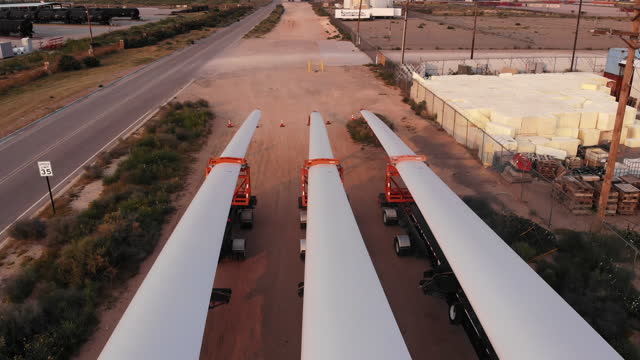 Sweeping Aerial View Of Wind Turbines Hauled By Extra Long Flatbed Semi-Trailer Trucks Across The Border From Mexico, Parked Side By Side