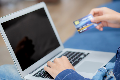 Hand of young man using laptop computer display blank screen shopping online with credit card on sofa at home, male purchase and payment with debit card, e-commerce and technology, lifestyle concept.