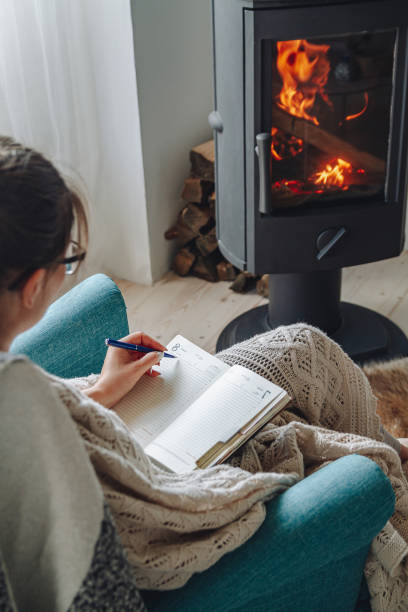 istock Young woman write in notebook sitting in armchair by fireplace 1341289628