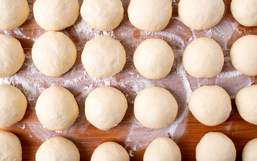 Yeast dough balls on the wooden board with flour. Preparing to bake buns, pizza or bread. Top view