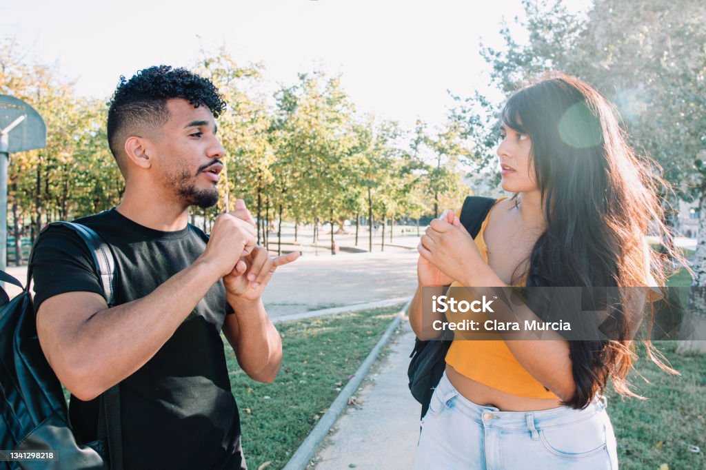 Sign language: 2 hispanic and african american student friends deaf  talking with nonverbal communication. Latinx deafness conversation. Sign Language Stock Photo