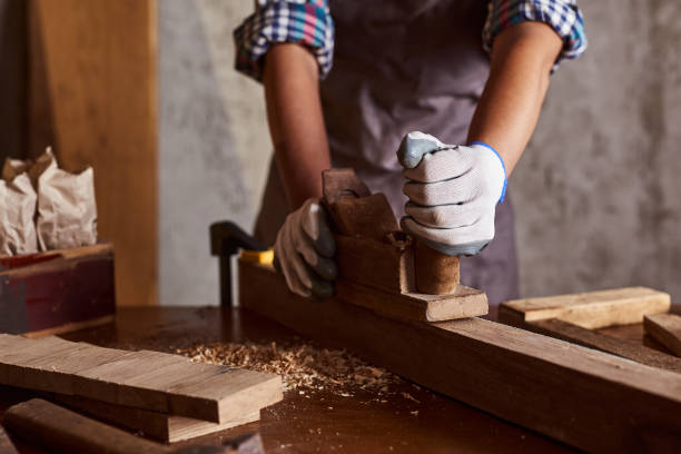 istock Female Apprentice Planing Wood In Carpentry Workshop. Carpenter woman working with plane. 1341299167