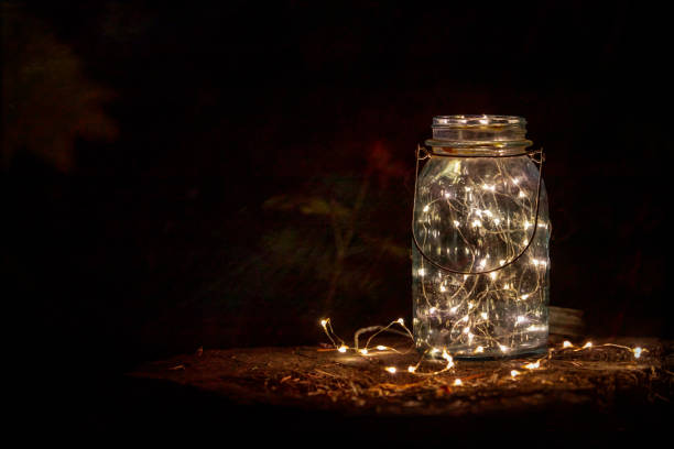 istock Mason Jar with twinkle lights on a log stump at night 1341303693