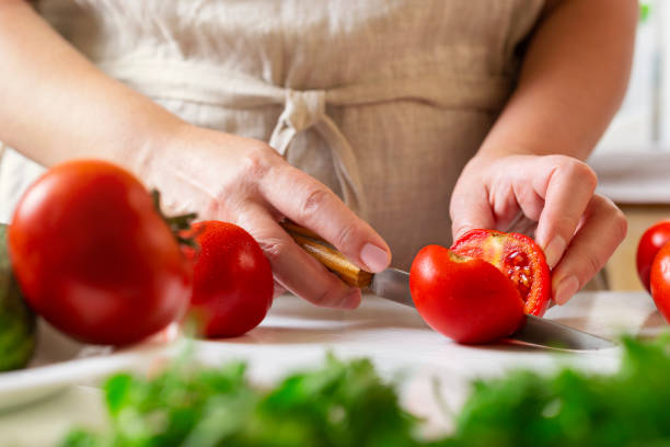 istock Chef slicing tomato using knife on the table in restaurant. Process of cutting and preparation food in kitchen. 1341305623