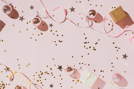 Pink background with confetti and Christmas shiny balls, flat lay. New Year celebration concept