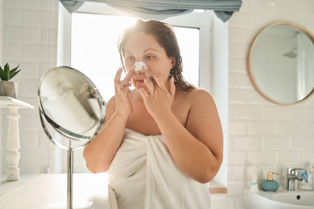Oversize woman applying nose strips in bathroom