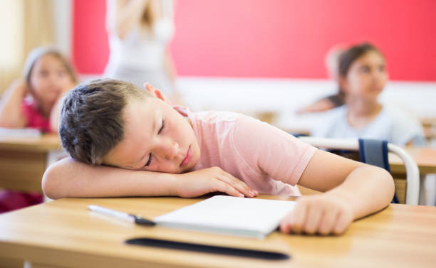 istock Tired school boy sleeping in classroom during lesson 1341311599
