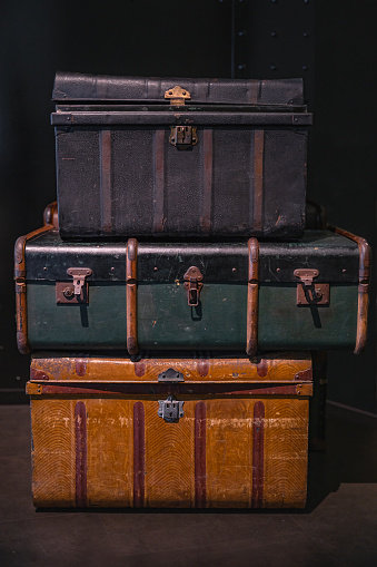 Selective focus on pile of three vintage, old and warn travel suitcases or trunks on the floor. Retro style voyage.