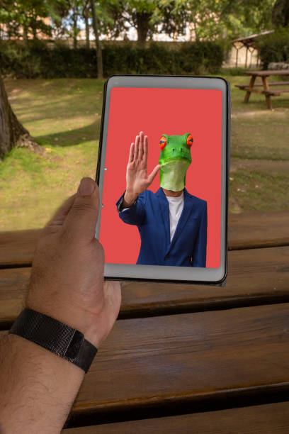 man holding a tablet in a garden with a wooden table and a picture of a man with a frog mask indicating stop - frog computer computer monitor symbol imagens e fotografias de stock