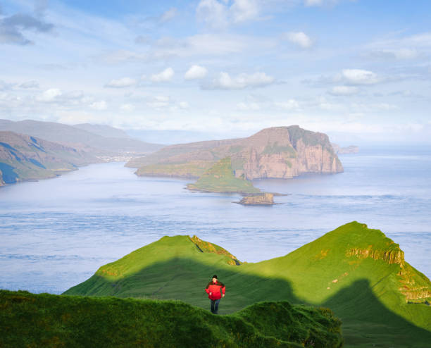 Tourist walks on Mykines with views of islands of Tindholmur and Vagar, Faroe A tourist walks on the island of Mykines overlooking the islands of Tindholmur and Vagar, Faroe Islands mykines faroe islands photos stock pictures, royalty-free photos & images