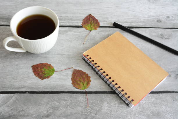 灰色の木製の背景にコーヒーと乾燥した紅葉の白いカップとノートと黒のペン - letter resume document writing ストックフォトと画像