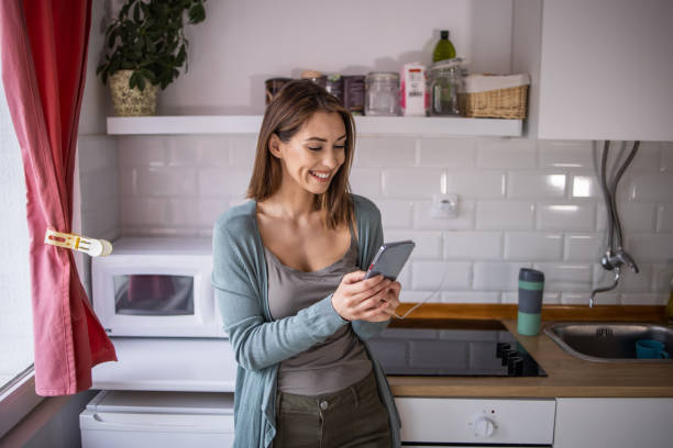 istock Smiling woman standing in kitchen and using mobile phone 1341319730