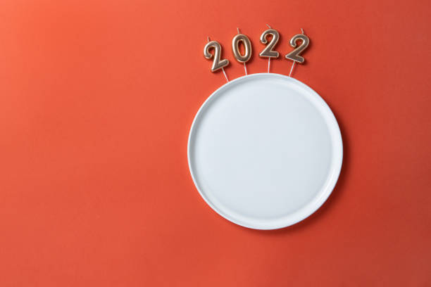 istock Creative Christmas table setting. Empty plate with straight edges, candles in form of numbers 2022, on red background, copy space, minimal layout, mockup. Concept for festive menu, diet, food 1341323834