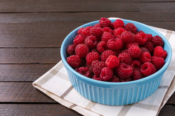 istock Red raspberry berry in plate on wooden table. 1341326290