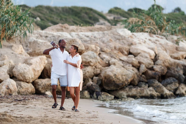 istock Happy mixed race, middle age couple embracing while walking on the beach holding a guitar. Man holding guitar with woman 1341331121