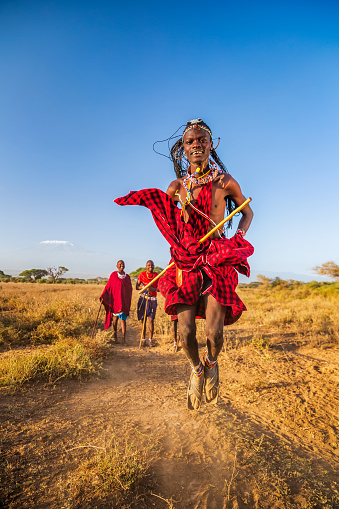 African warrior from Maasai tribe performing a traditional jumping dance, central Kenya, Africa - Mount Kilimanjaro on the background. Maasai tribe inhabiting southern Kenya and northern Tanzania, and they are related to the Samburu.