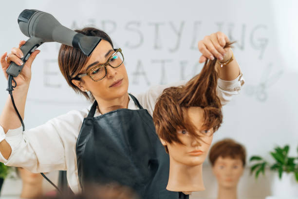 istock Hairstylist with the Hair Dryer in Hands Explaining Hairstyling Techniques, Using Mannequin Head 1341333896