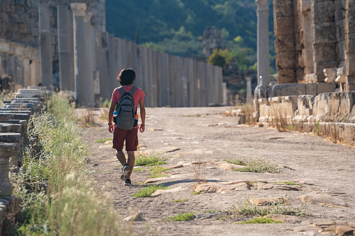 Photo of travelling young adult man with backpack in antique city of Perge, Antalya, Turkey. Shot under daylight with a full frame mirrorless camera and a tele photo lens.