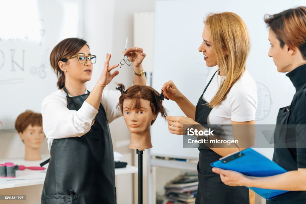 Hairdressers Training with Mannequin Head in Education Center Hairdressers Training with Mannequin Head in Education Center. Professional female hairdresser teaching adult students haircutting technique. Hairdresser Stock Photo