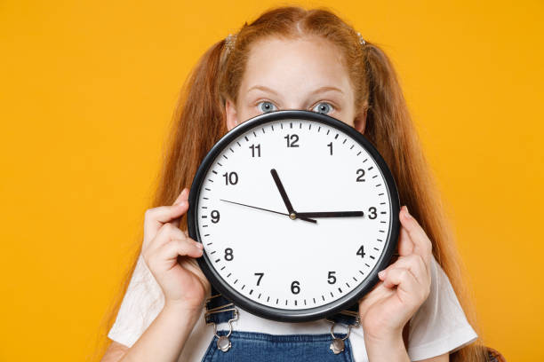 young redhead school teen kid girl 12-13 years old in white t-shirt blue denim uniform backpack hold in hands clock isolated on yellow background children studio portrait education lifestyle concept - 12 13 years fotos imagens e fotografias de stock
