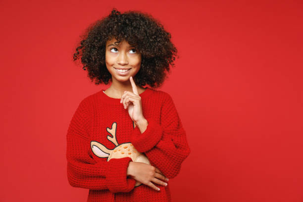 little african curly kid girl 12-13 years old wearing knitted cozy deer christmas sweater think dream make wish isolated on bright red background children studio portrait childhood lifestyle concept - 12 13 years fotos imagens e fotografias de stock
