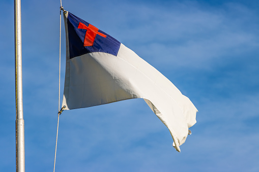 A Christian religious flag flies outside of a church on a sunny day.