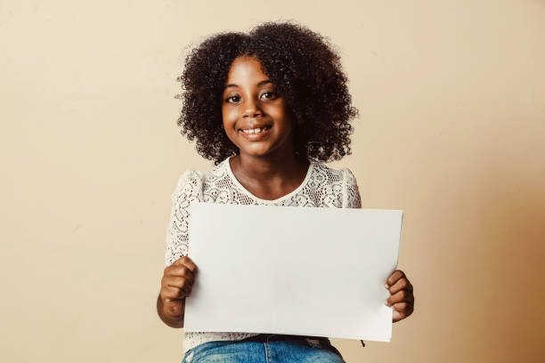 маленькая девочка черная с афро-волосами, держащая плакат. ребенок смотрит в камеру, держащую плакат. - african descent child little girls african ethnicity стоковые фото и изображения