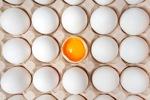 White eggs with one broken egg in carton box. Eggs background. Food concept. Flat lay, top view.