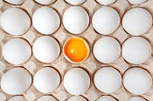 White eggs with one broken egg in carton box. Eggs background. Food concept. Flat lay, top view.