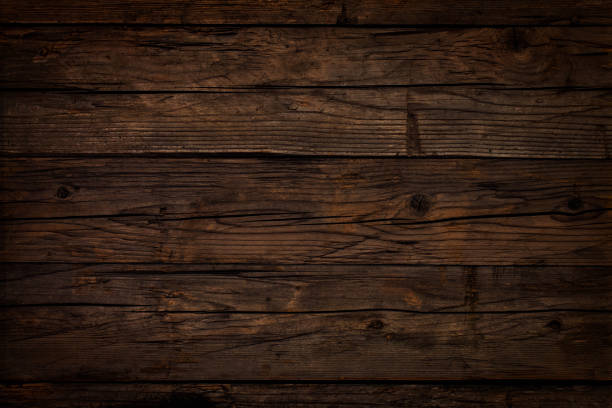 Old dark brown wooden board Old weathered dark wooden table board. Wood knots, cracks, stains, scratches and other damages are strongly expressed. All planks have a strong clear texture of wood. A wood grain pattern featuring even grains of wood running horizontally across the image. Compounds of the planks are clearly visible. timber stock pictures, royalty-free photos & images
