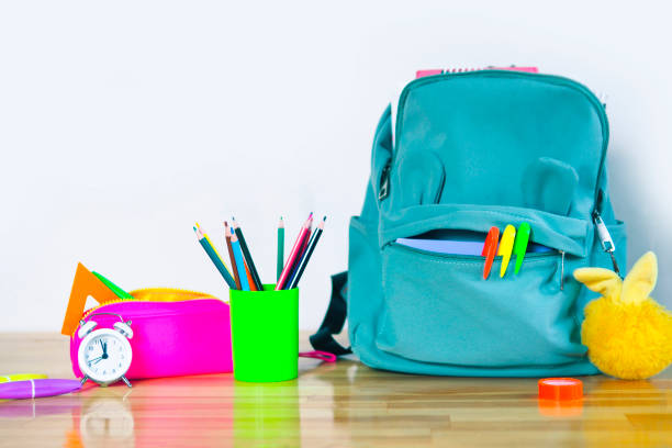 istock funny school backpack with markers, bright pencil case, fluffy keychain glass with colored pencils and an alarm clock on a wooden table. back to school concept. 1341360483