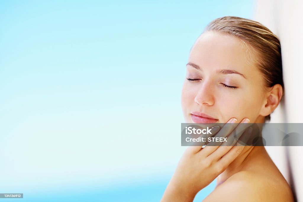 Jovem mulher tocando seu rosto enquanto inclinando-se contra uma parede - Foto de stock de 20 Anos royalty-free